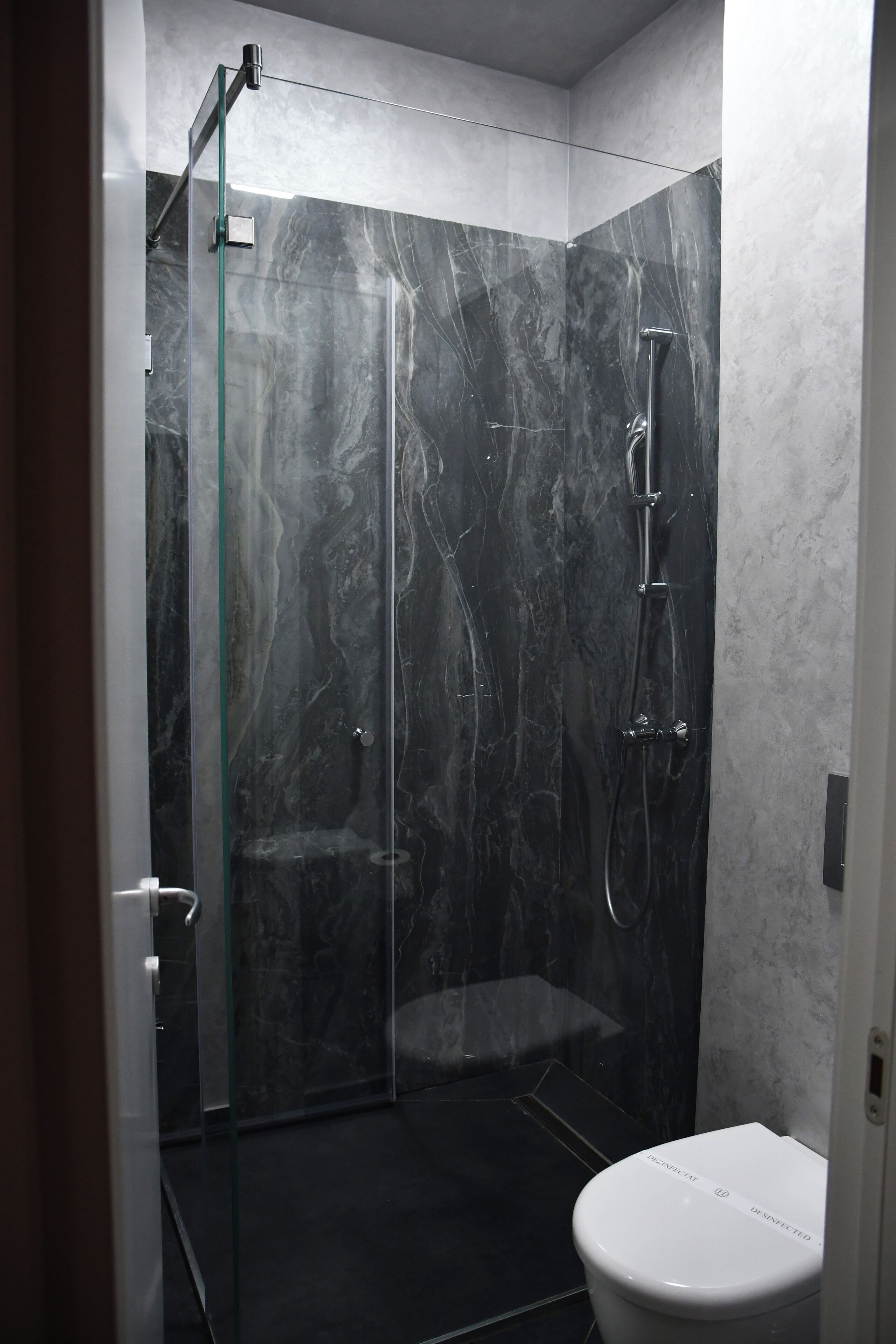 A modern bathroom with a glass-enclosed shower, a white toilet, and marble walls.