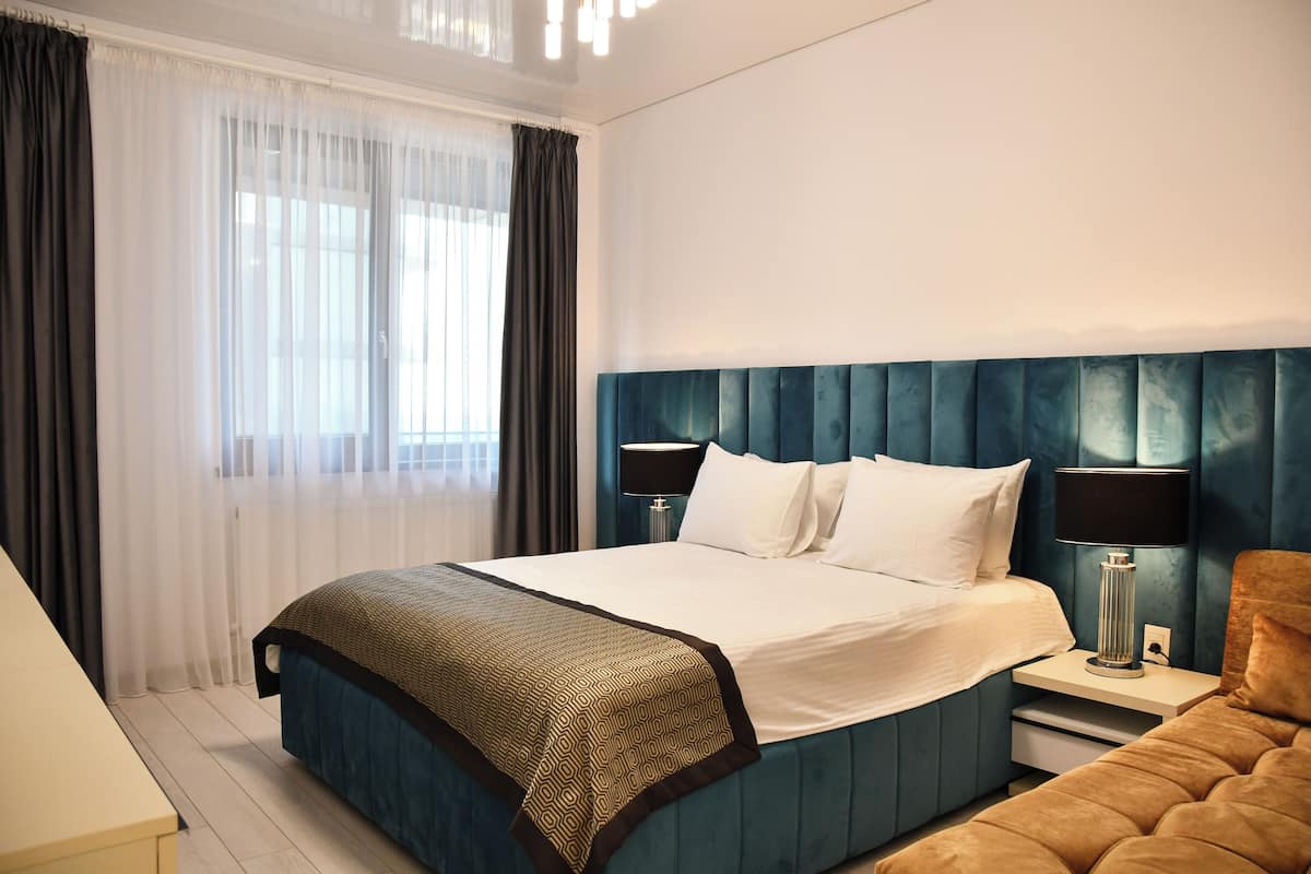 A modern hotel room with a large bed, a nightstand with a lamp, and a view of the city through the window.