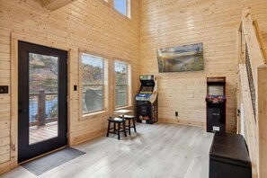 Interior de madera con dos ventanas, una puerta, una mesa pequeña y dos máquinas de arcade.
