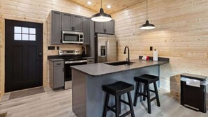 A modern kitchen with grey cabinets, stainless steel appliances, and a central island with bar stools. - Black Bear by Beyond Expectations: 2BR Cabin w/ Hot Tub, Arcade, & Axe Throwing (Sevierville)