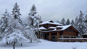 Eine Blockhütte mit Steinfundament, umgeben von schneebedeckten Bäumen.