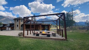 Eine rustikale Holzhütte mit Steinunterbau und Holzfassade, umgeben von einer Wiese mit Feuerstelle und Holzbänken.