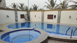 A swimming pool with a hot tub and a small water feature, surrounded by a tiled deck and palm trees. - Apno Hotel and Suites  (Lekki)
