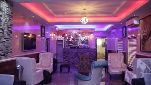 A bar area with a stone wall, bar counter, and seating with chairs and a sofa. - Apno Hotel and Suites  (Lekki)