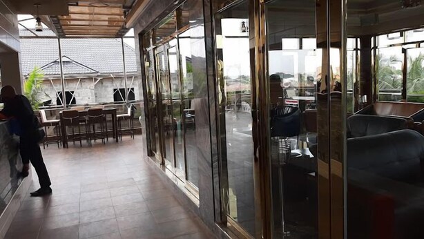 An indoor seating area with tables and chairs, large windows, and a view of the outside. - Apno Hotel and Suites  (Lekki)