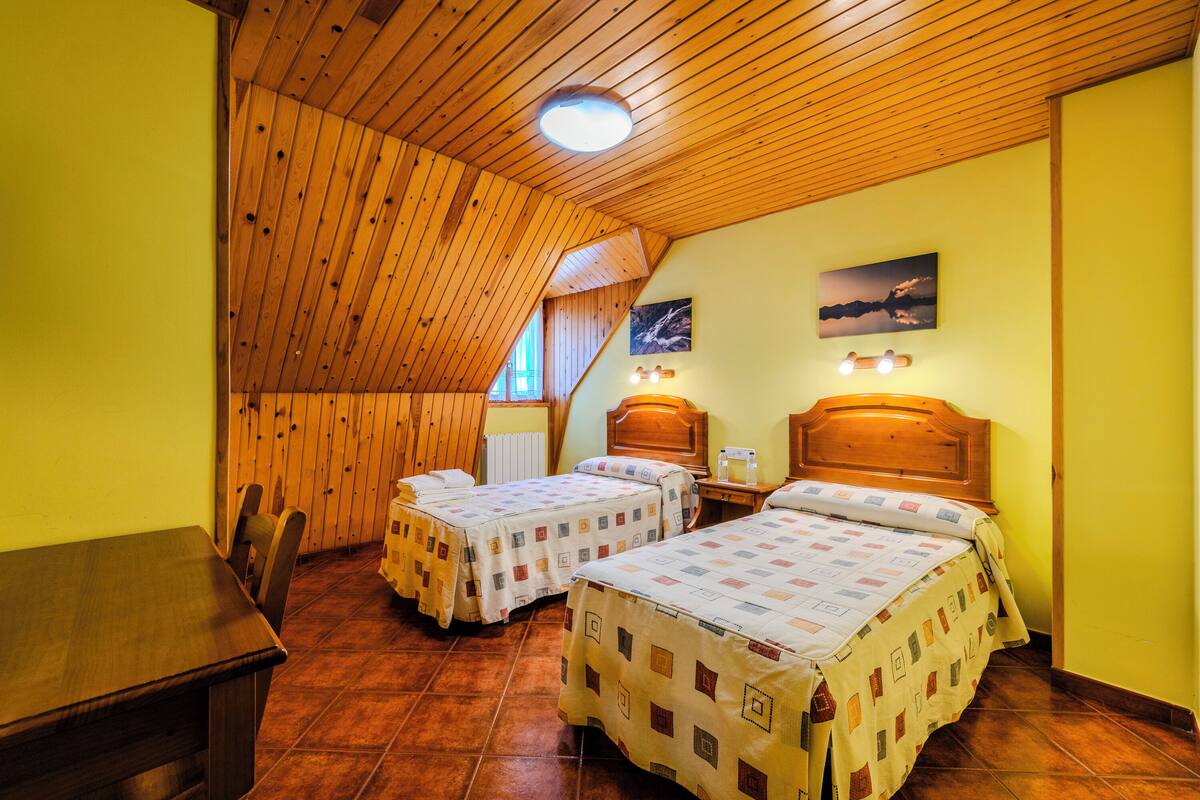 A room with two beds, wooden ceiling, and a dining table.