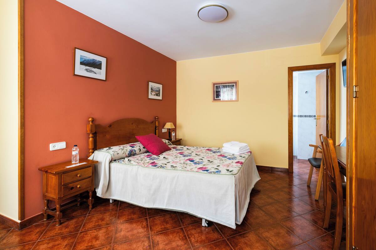 A bedroom with a wooden bed, a nightstand, a bedside table, and a chair.