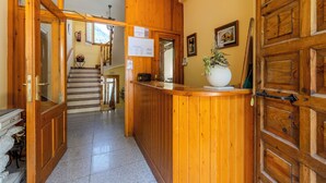 A wooden reception desk with a potted plant, a staircase, and a framed picture on the wall.
