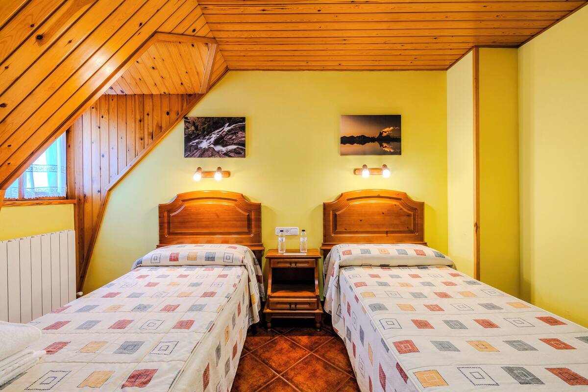 A room with two beds, wooden headboards, and a sloped ceiling.