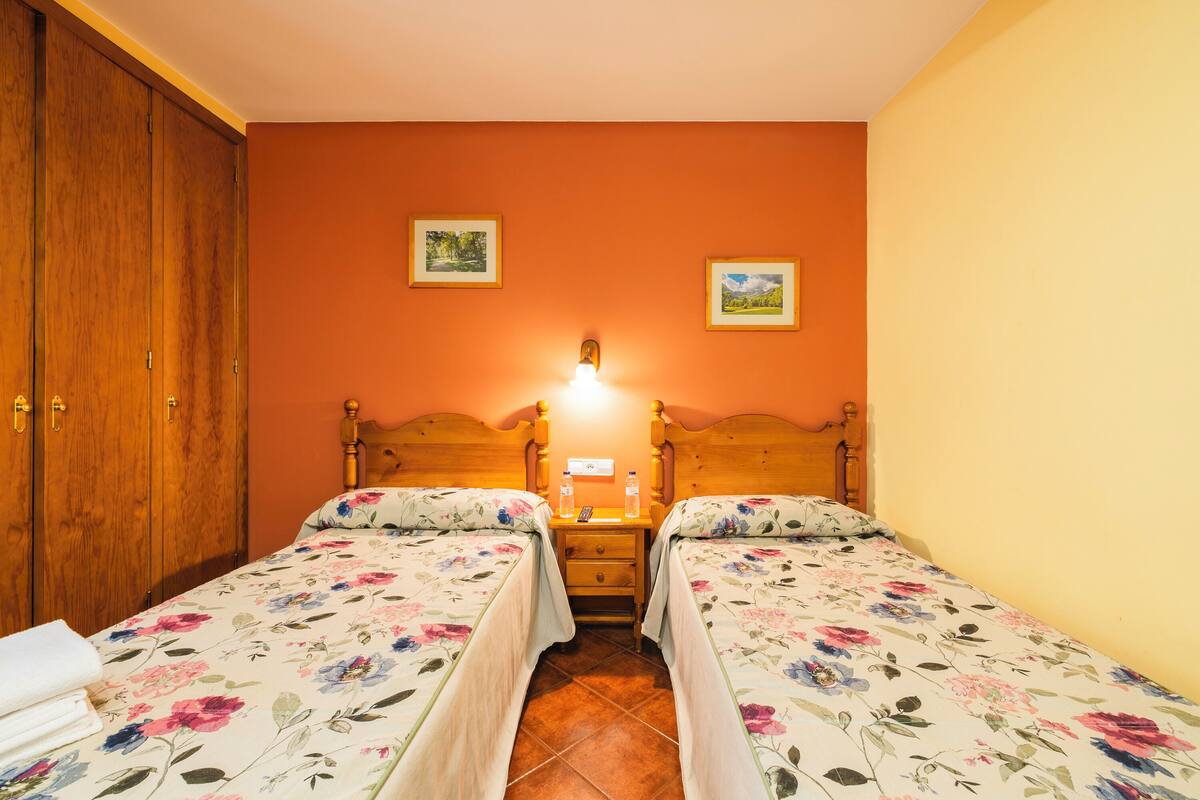 A bedroom with two single beds, wooden headboards, a nightstand with a lamp, and two framed pictures on the wall.
