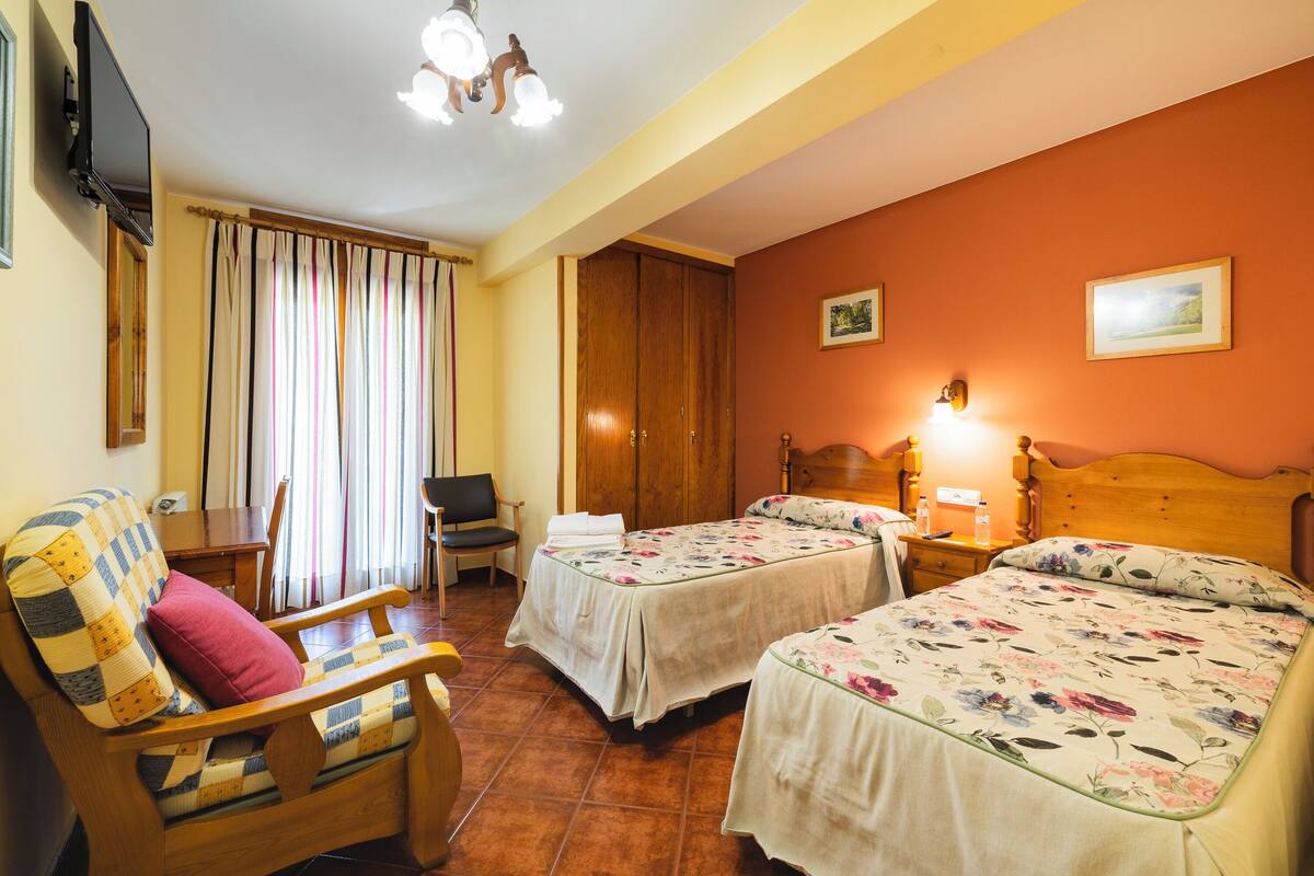 A hotel room with two beds, a wooden chair, a desk, and a television.