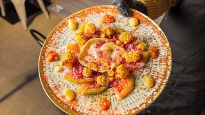 A plate of food with various toppings and a person holding a black glove.