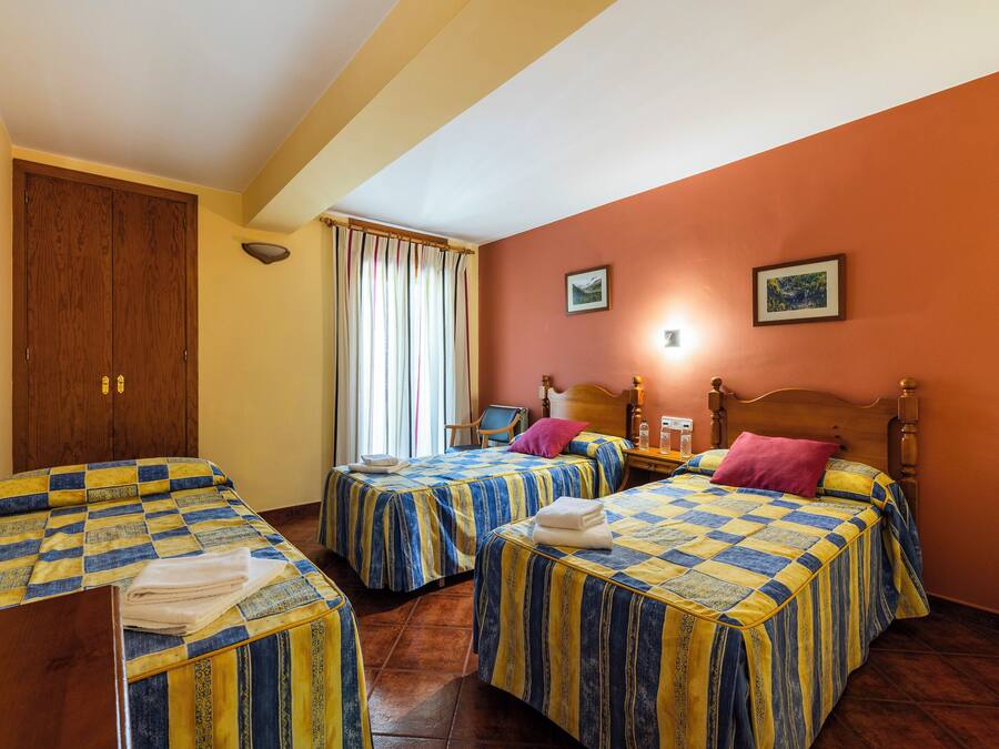 A hotel room with two beds, wooden headboards, a wooden wardrobe, a chair, and a window with curtains.
