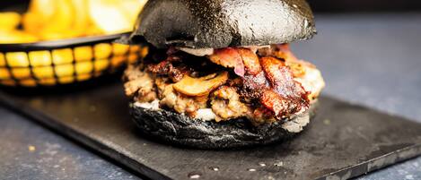 A burger with bacon and mushrooms on a black bun, served with fries on a black tray.