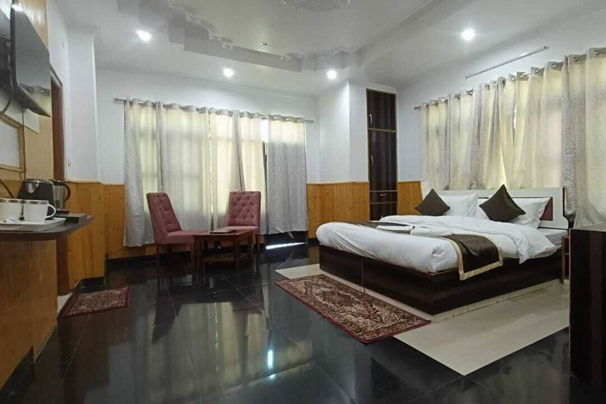 A hotel room with a large bed, two chairs, a wardrobe, and a television.
