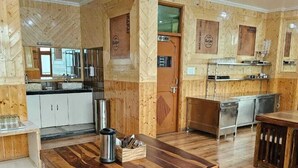 A spacious kitchen with wooden cabinetry, a central island, and a dining area with a wooden table and chairs. - Hotel Sarahan Inn (Rampur)