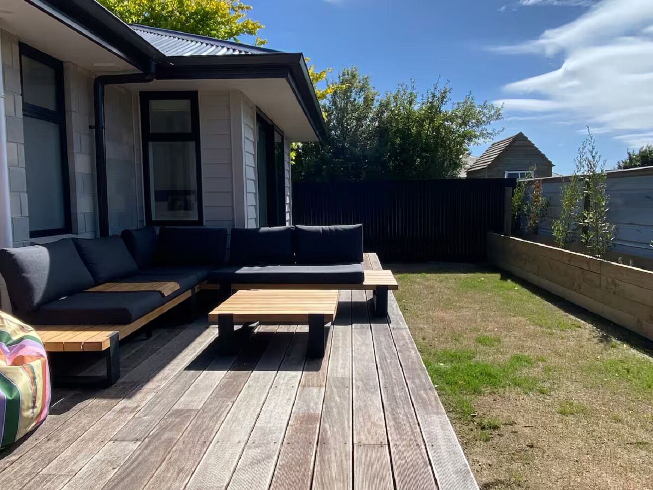 Eine Holzterrasse mit einer Couch und einem Tisch, umgeben von einem Holzzaun und einem Haus.