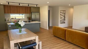 A modern kitchen with a built-in refrigerator, a dining table with a vase of flowers, and a yellow sofa in a living area with wooden flooring.