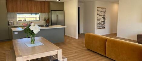A modern kitchen with a built-in refrigerator, a dining table with a vase of flowers, and a yellow sofa in a living area with wooden flooring.
