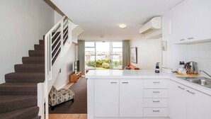 A modern kitchen with white cabinets, a central island, and a staircase leading to a balcony with a city view. - Wake up to spectacular harbour views and watch ships glide past from your private balcony. <br>Mariners Lookout is a spacious waterfront apartment just minutes from Fremantle's cafés, restaurants, Bathers Beach and the Rottnest Ferry. <br>Perfect for (Fremantle)