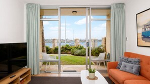 A modern living room with a TV, sofa, and a view of a marina. - Wake up to spectacular harbour views and watch ships glide past from your private balcony. <br>Mariners Lookout is a spacious waterfront apartment just minutes from Fremantle's cafés, restaurants, Bathers Beach and the Rottnest Ferry. <br>Perfect for (Fremantle)