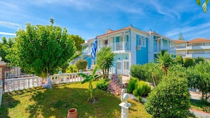 A two-story building with a balcony, surrounded by lush greenery and a clear blue sky. - Stathis Rooms (Zakynthos)