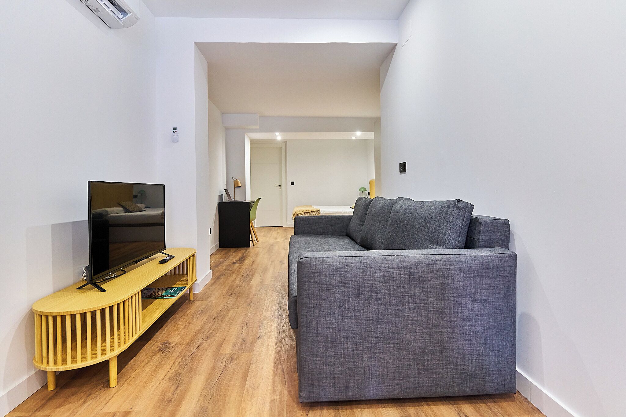 A modern living room with a grey sofa, wooden entertainment unit, and a flat-screen TV.