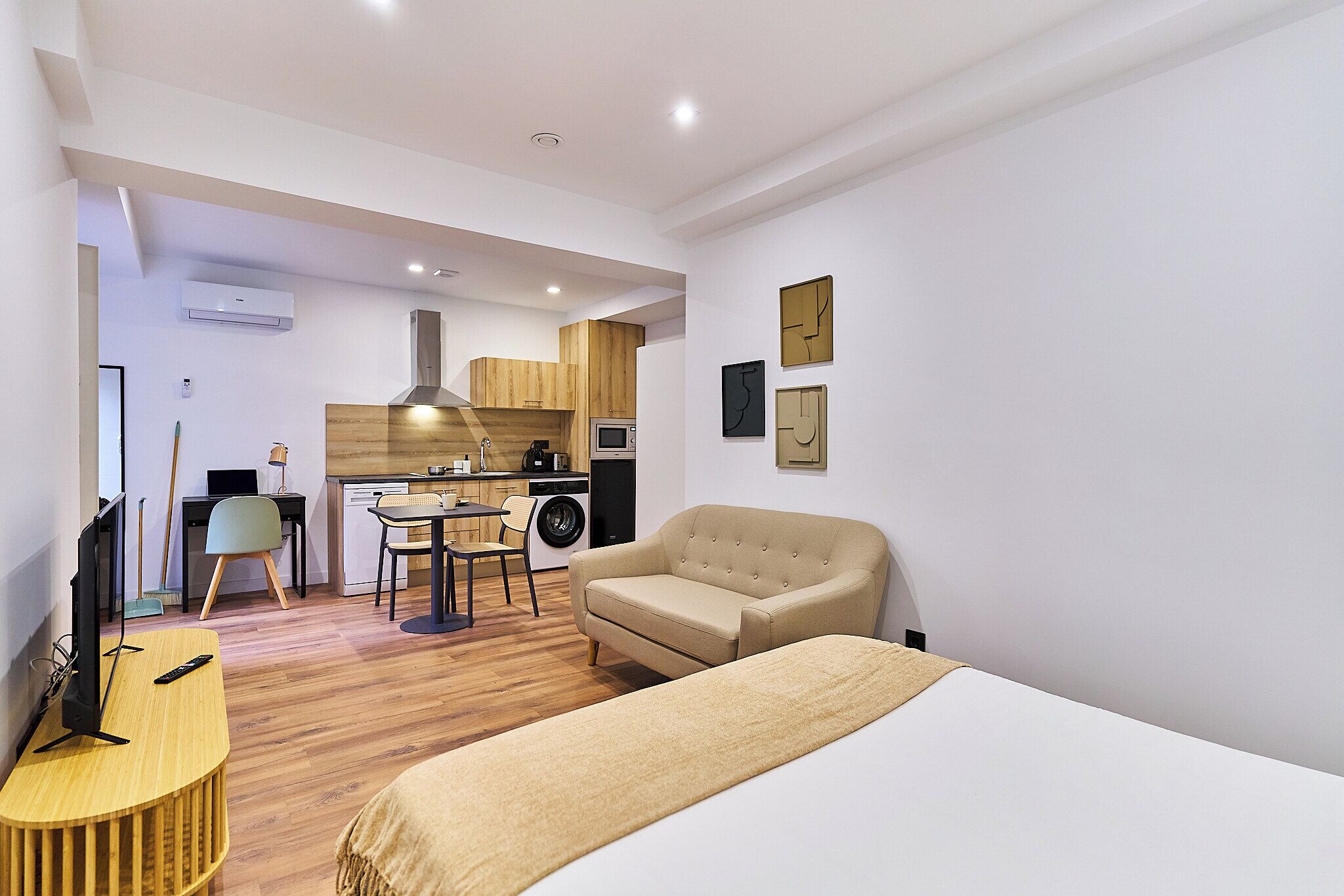 Una habitación moderna y bien iluminada con cama, escritorio, silla y una pequeña cocina.