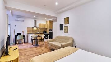 Una habitación moderna y bien iluminada con cama, escritorio, silla y una pequeña cocina.