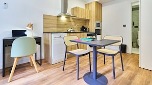 Cocina compacta con armarios de madera, microondas y lavavajillas. Hay una mesa de comedor con dos sillas.