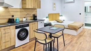 Una cocina compacta con lavadora, un comedor con dos sillas y una cama con cabecera.