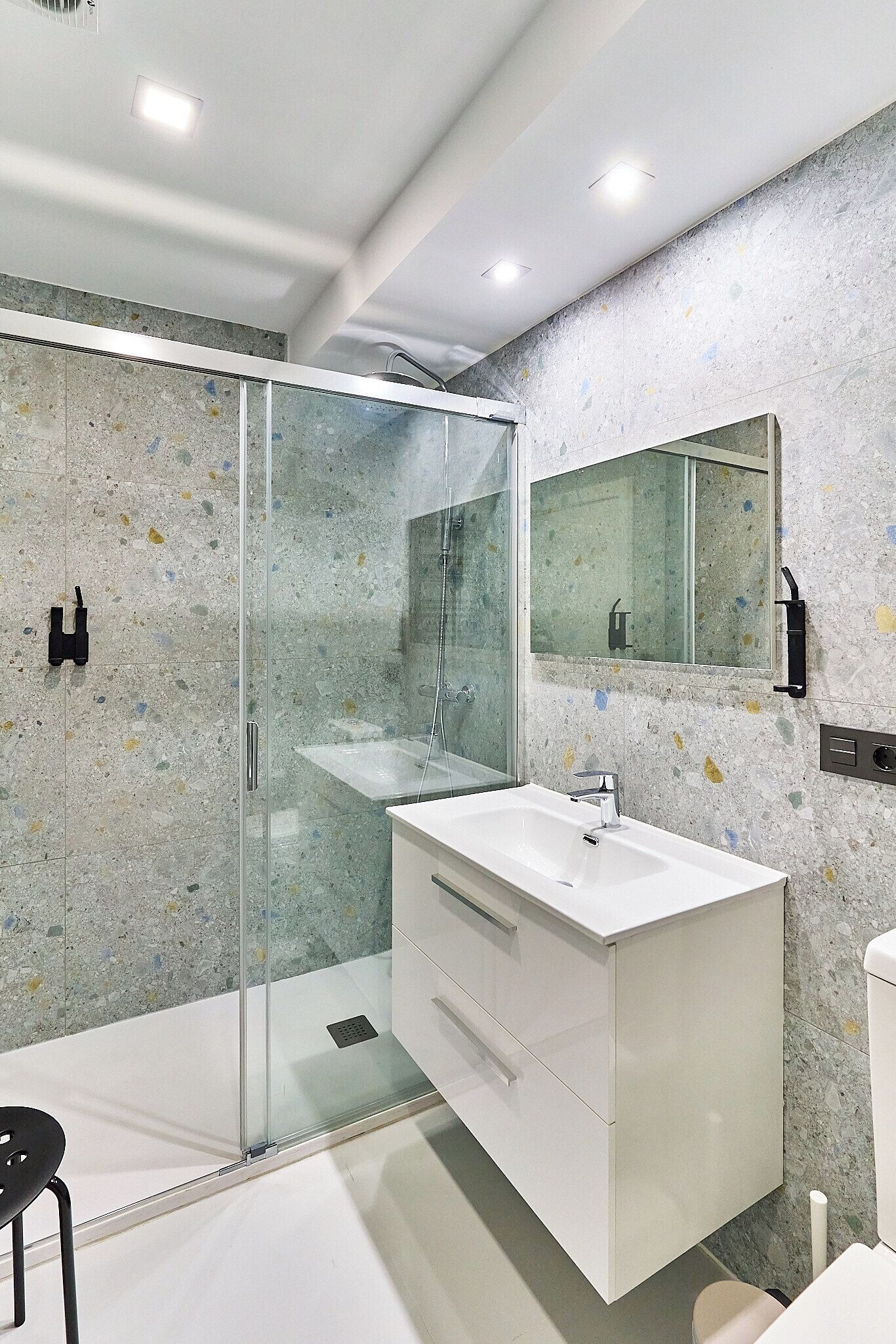 Un baño moderno con ducha envuelta en vidrio, un lavabo blanco y un espejo grande.