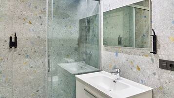 Un baño moderno con ducha envuelta en vidrio, un lavabo blanco y un espejo grande.