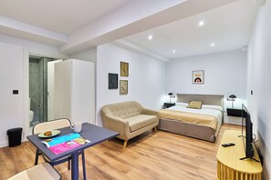 A modern hotel room with a bed, sofa, dining table, and a small TV. - Apartamentos Beatriz by gaiarooms (Salamanca)
