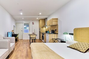 A compact hotel room with a bed, a small kitchenette, a dining area, and a view of the outside. - Apartamentos Beatriz by gaiarooms (Salamanca)