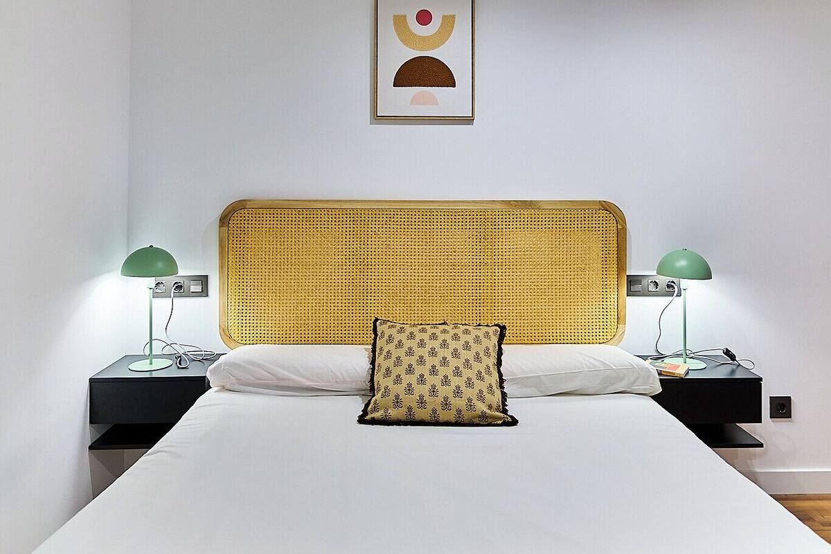 A neatly made bed with a yellow headboard, two bedside tables with lamps, and a framed picture on the wall.