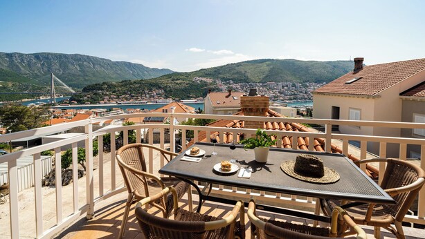 A balcony with wicker chairs and a table set for two, overlooking a coastal town and mountains. - Charming 2-bedroom apartment with AC, WiFi in enchanting Dubrovnik (Dubrovnik)