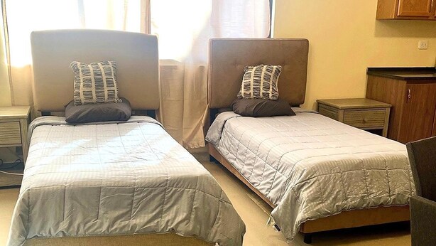 A hotel room with two beds, a small table, a chair, and a window with curtains. - mount houssein (Amman)