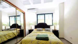 A bedroom with a large mirror, two bedside tables, a bed with a floral bedspread, and a window with blinds. - mount houssein (Amman)