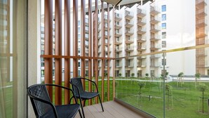 Een balkon met twee zwarte stoelen, uitzicht op een woongebouw en een gazon met kleine bomen.