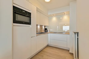 A modern kitchen with white cabinetry, a built-in oven, a coffee maker, and a refrigerator. - Apartment in Blankenberge With Sea Views (Blankenberge)