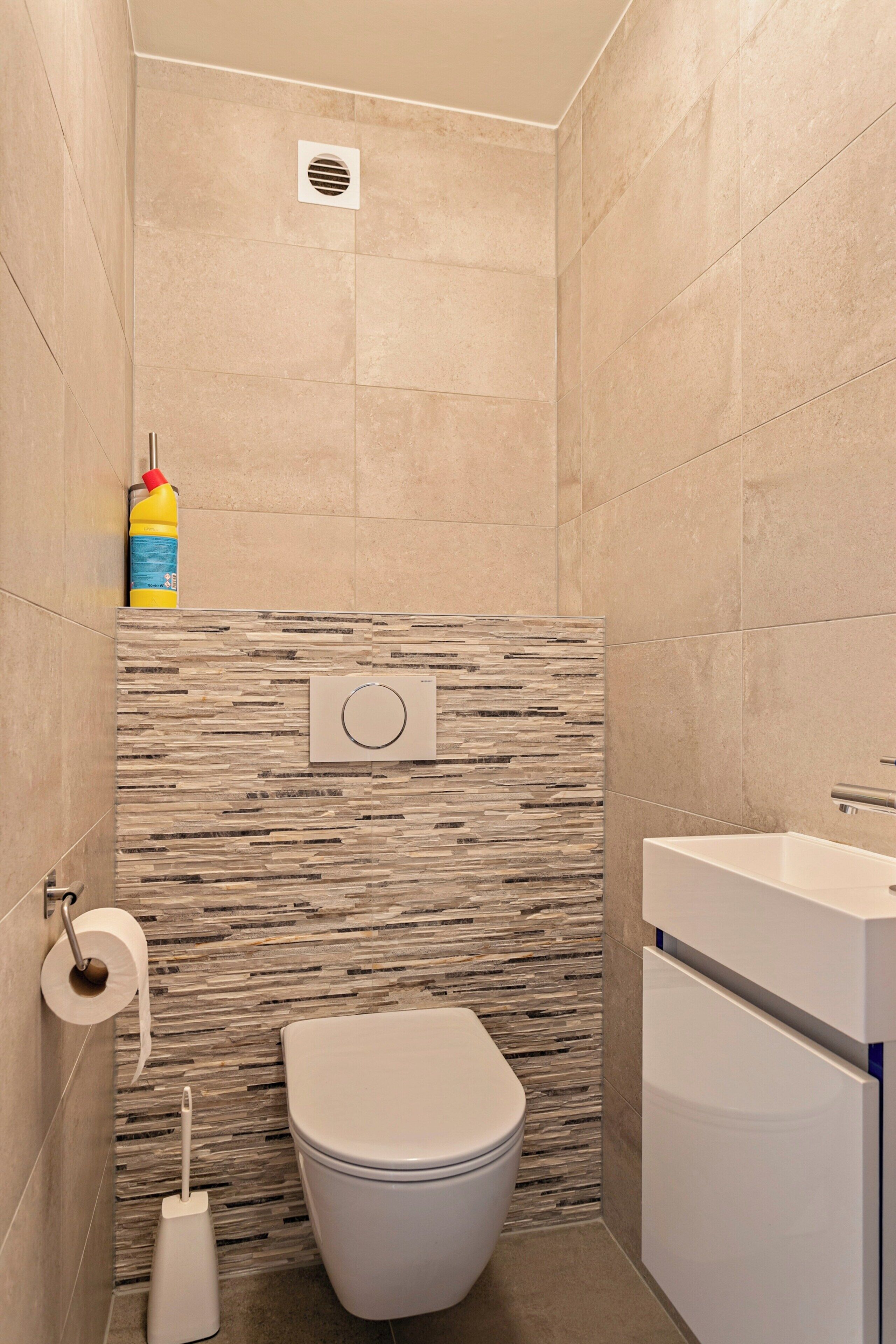 Egy modern fürőszoba, amelyben WC, mosdókagyló és zuhanyzó található.