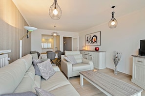 A modern living room with a sofa, armchair, coffee table, and pendant lights. - Apartment in Blankenberge With Sea Views (Blankenberge)