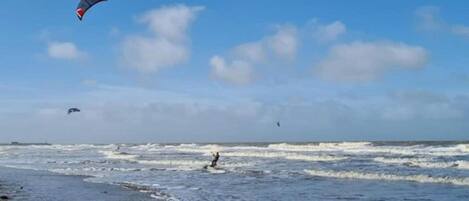 Una spiaggia con onde e una persona che fa kitesurf.