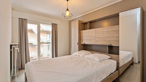 Un dormitorio moderno con una cama grande, almacenamiento integrado, vistas al balcón exterior y una lámpara colgante geométrica única.