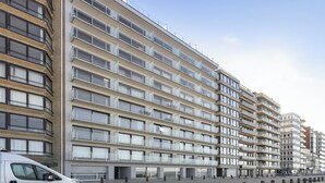 Un edificio residencial de varios pisos con balcones, una zona de estacionamiento y cielo despejado.