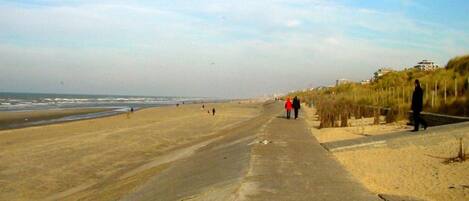 A beach with a concrete walkway, people walking, and buildings in the background.