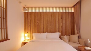 A hotel room with a large bed, a bedside table with a lamp, a small seating area, and a wooden headboard. - Hantang Inn Hostel Xi'an (Xi'an)