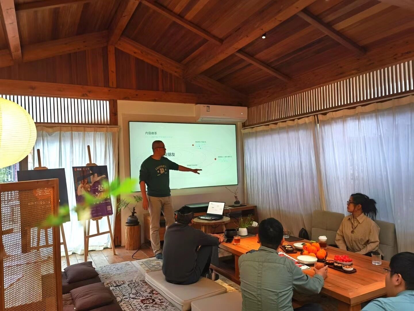 Una sala de reuniones con techo de madera, una pantalla para proyector, una computadora portátil y una mesa con comida y bebidas.