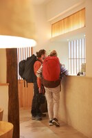 Two people standing in a hallway with wooden paneling and a reception desk.